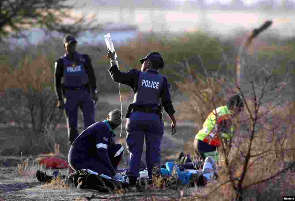 A paramedic (front L) receives help from a policewomen as he tends to the injured after protesting miners were shot outside a South African mine in Rustenburg, August 16, 2012.