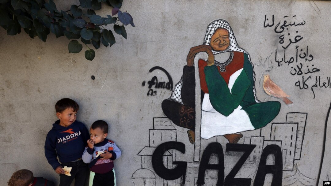 Displaced Palestinian children stand next to a mural painting by artist Amal Abo in Rafah in the southern of Gaza Strip, on Dec. 31, 2023.