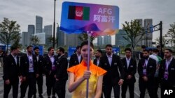 在中國杭州舉行的第19屆亞運會歡迎儀式上，一名志願者舉牌站在阿富汗塔利班政權派出的全部為男性運動員的隊伍前。（2023年9月20日）