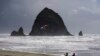 FILE - Beachgoers fly a kite by Haystack Rock in the Pacific Ocean off the Oregon Coast, April 4, 2022. On Saturday, which has been designated World Oceans Day, groups will try to raise awareness about what the oceans do for the Earth and what humans are doing to the oceans. 