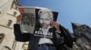 FILE - A demonstrator, holding a poster protesting the possible extradition to the U.S. of WikiLeaks founder Julian Assange, reads a newspaper outside the High Court in London, May 20, 2024.