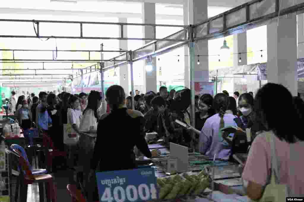 អ្នកចូលរួមកំពុងឈរទិញសៀវភៅក្នុងស្តង់សៀវភៅមួយកន្លែងក្នុងកម្មវិធីពិព័រណ៌សៀវភៅក្នុងទិវាជាតិអំណានលើកទី៩ នៅវិទ្យាស្ថានបច្ចេកវិទ្យាកម្ពុជា ក្នុងរាជធានីភ្នំពេញ នាថ្ងៃទី៩ ខែមីនា ឆ្នាំ២០២៤។ (សើ ដាវី/វីអូអេ)