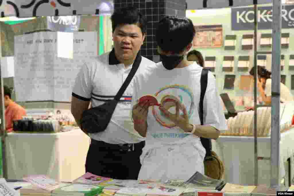 បុរសពីរនាក់កំពុងឈរមើលសៀវភៅក្នុងស្តង់សៀវភៅមួយកន្លែងក្នុងកម្មវិធីពិព័រណ៌សៀវភៅក្នុងទិវាជាតិអំណានលើកទី៩ នៅវិទ្យាស្ថានបច្ចេកវិទ្យាកម្ពុជា ក្នុងរាជធានីភ្នំពេញ នាថ្ងៃទី៩ ខែមីនា ឆ្នាំ២០២៤។ (ស៊ឹម ចាន់សំណាង/វីអូអេ)