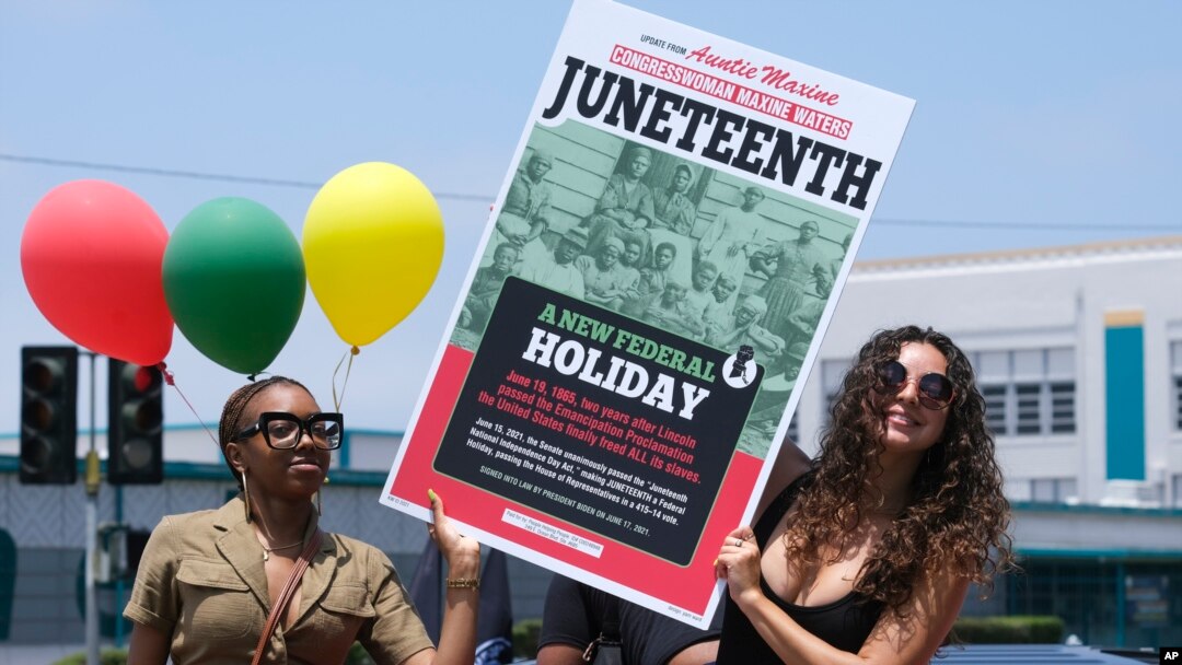 Dos personas sostienen un cartel desde su automóvil durante un desfile para conmemorar el 19 de junio de 2021, en Inglewood, California.