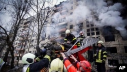Des pompiers ukrainiens évacuent un homme d'un immeuble touché par un bombardement à Kiev, en Ukraine, le lundi 14 mars 2022, lors du conflit entre la Russie et l'Ukraine. (Photo AP/Service d'urgence de l'État ukrainien)