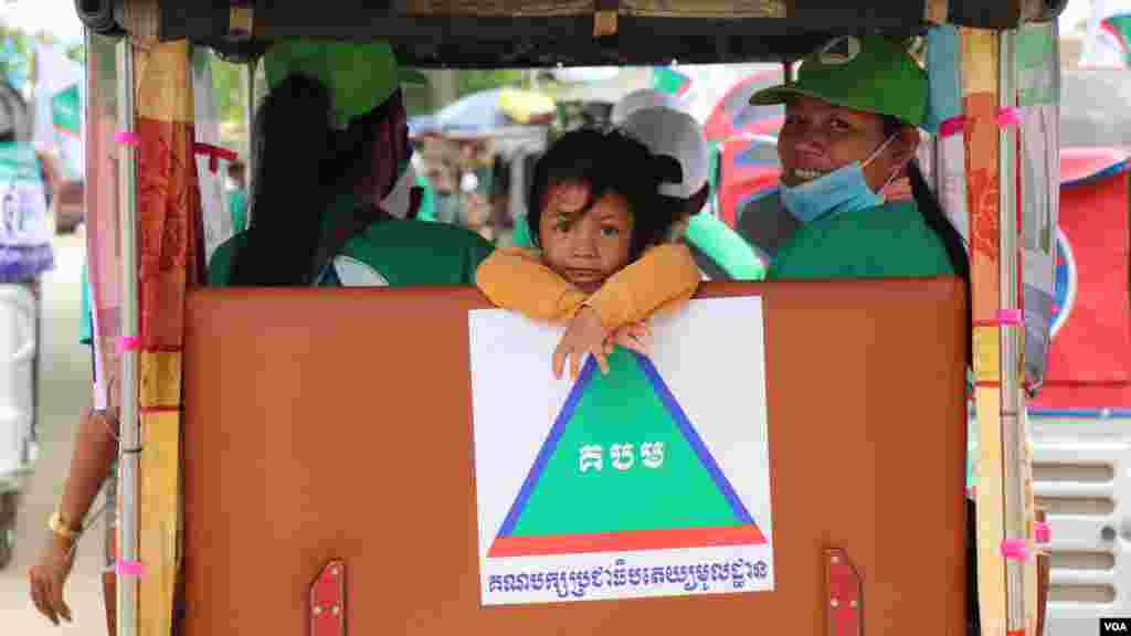 កូនស្រីរបស់អ្នកគាំទ្រគណបក្សប្រជាធិបតេយ្យមូលដ្ឋាន ជិះកង់បីជាមួយម្តាយ ដើម្បីឃោសនាគោលនយោបាយបក្ស នៅក្នុងសង្កាត់កោះដាច់ ខណ្ឌជ្រោយចង្វារ នៅថ្ងៃទី២១ ខែឧសភា ឆ្នាំ២០២២។ (លាស់ លីបលីប/វីអូអេ)