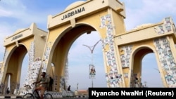 Un homme passe à vélo devant un monument décoré d'affiches électorales à Yola, dans l'État d'Adamawa, au Nigeria, le 26 février 2019. 