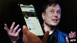 Un écran de téléphone affiche le compte Twitter d'Elon Musk avec une photo de lui en arrière-plan, le 14 avril 2022, à Washington DC.