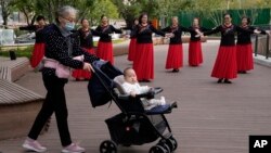 資料照：一名老年婦女推著一個嬰兒走過北京一所公園裡跳廣場舞的婦女。（2021年10月14日）