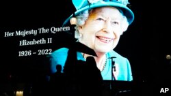 People pass by an image of Queen Elizabeth II projected onto a large screen at Piccadilly Circus, in London, Sept. 8, 2022.
২০২২ সালের ৮ সেপ্টেম্বর লন্ডনের পিকাডিলি সার্কাসে ২০২২ সালের ৮ সেপ্টেম্বর একটি বড় পর্দায় রানী দ্বিতীয় এলিজাবেথের প্রদর্শিত একটি ছবি।