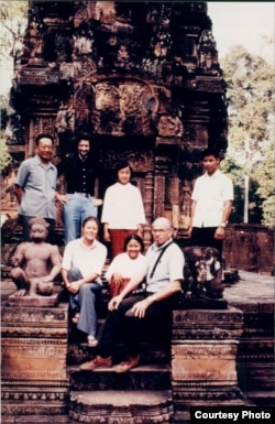 The color photograph of the group includes Richard Dudman (bald), Malcolm Caldwell (flowing hair) and Elizabeth Becker in front of a temple at Angkor Wat. With them are two young aides and Thiounn Prasith, a senior Khmer Rouge official at the Ministry of Foreign Affairs. (Courtesy photo of Elizabeth Becker)