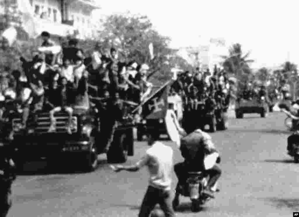 ក្បួនរថយន្តទាហានខ្មែរក្រហមដោយមានគ្រវីទង់ជ័យផង បើកចូលភ្នំពេញកាលពីថ្ងៃទី១៧ ខែមេសា ឆ្នាំ១៩៧៥ នៅពេលរដ្ឋធានីនៃសាធារណរដ្ឋខ្មែរត្រូវធ្លាក់ក្នុងដៃក្រុមខ្មែរក្រហម។ អ្នកទីក្រុងបើកម៉ូតូកាត់ក្បួនរថយន្តទាហានខ្មែរក្រហម។ (AP Photo)