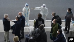 世衛組織的專家抵達武漢天河國際機場，身穿防護服的中國工作人員給他們指方向。（2021年1月14日）