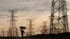 FILE - A woman carries firewood on her head as she walks below Eskom's electricity pylons in Soweto, South Africa, Aug. 8, 2016.