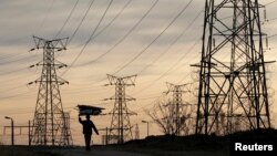 FILE - A woman carries firewood on her head as she walks below Eskom's electricity pylons in Soweto, South Africa, Aug. 8, 2016.