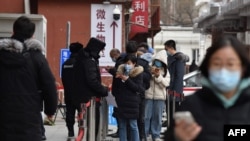 2021年1月14日人們在北京一家醫院排隊測試新冠病毒時通過手機刷健康碼。（法新社提供）