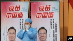 北京一位醫護人員站在“疫苗中國造”宣傳畫前。 （2021年4月9日）