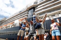 FILE - Passengers react after they disembark from the MS Westerdam, back, at the port of Sihanoukville, Cambodia, Friday, Feb. 14, 2020. Hundreds of cruise ship passengers long stranded at sea by virus fears cheered as they finally disembarked Friday.