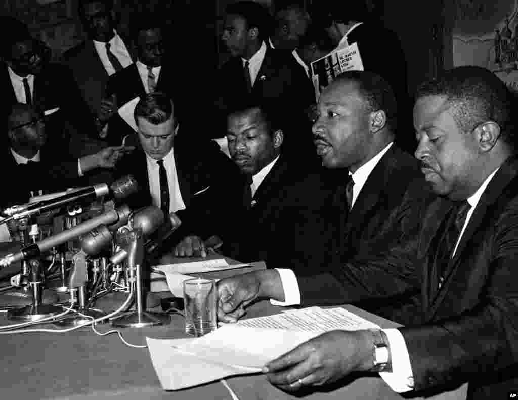 លោក Martin Luther King, Jr. ថ្លែងនៅក្នុងសន្និសីទកាសែតមួយ នៅក្បែរលោក John Lewis ដែលជាប្រធាននៃគណៈកម្មាធិការសម្របសម្រួលអំពើអហិង្សារបស់និស្សិត នៅក្នុងក្រុង Baltimore រដ្ឋ Maryland កាលពីថ្ងៃទី២ ខែមេសា ឆ្នាំ១៩៦៥។