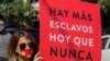 Una mujer sostiene un cartel que reza "Hay más esclavos ahora que nunca" mientras se une a cientos con camisas negras y cinta roja en la boca durante la tercera edición anual de la 'Caminata por la libertad' contra la esclavitud moderna, en México.