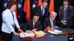 Australian Prime Minister Tony Abbott, back center, watches as China's Minister of Commerce Gao Hucheng, second left, and Australian Minister for Trade Andrew Robb, second right, sign a free trade agreement between the two countries in Canberra, Australia