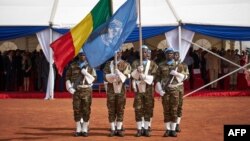 Des soldats brandissent les drapeaux de l'ONU et du Mali lors de la cérémonie de la Journée des Casques bleus à la base opérationnelle de la Minusma à Bamako, le 29 mai 2018.