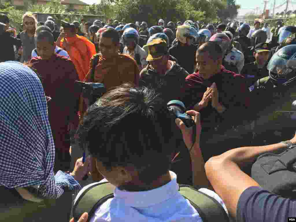 A group of Cambodian monks hold a Buddhist ceremony for protesters killed in early 2014, as police and security personnel are seen surrounding the group, on Sunday, January 03, 2016. (Hul Reaksmey/VOA Khmer) 
