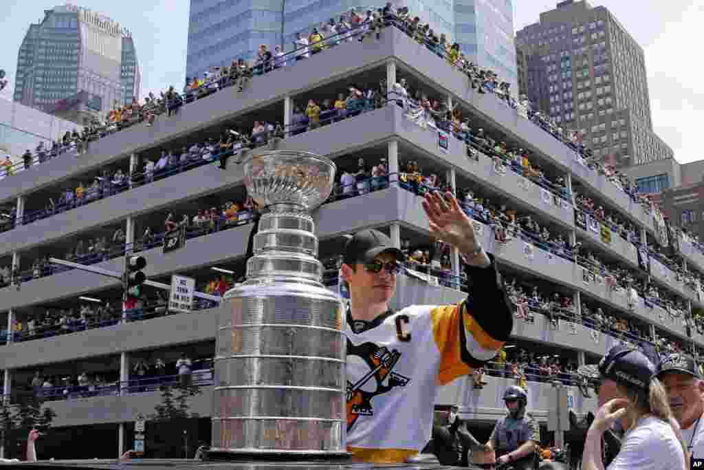 在美国匹茨堡举行的斯坦利杯胜利游行中,匹茨堡企鹅队队员Sidney Crosby 在斯坦利杯(Stanley Cup)旁边挥手致意。(2017年6月14日)