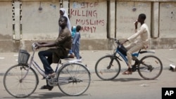 Deux hommes à vélos passe devant le message "Stop killing Muslims Army" (Arrêter de tuer les militaires musulmans) sur un mur à Kano, Nigeria, le 8 avril 2016. 
