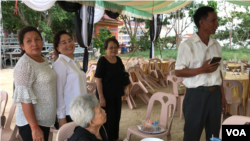 អ្នកស្រី ឡៅ ជាលីនដា (អាវស) ឈរស្វាគមន៍ភ្ញៀវមកចូលរួមបុណ្យសព នួន ជា ជាឪពុក នៅវត្តព្រំគីរីមរកត ស្រុកសាលាក្រៅ ខេត្តប៉ៃលិន កាលពីថ្ងៃទី០៧ ខែសីហា ឆ្នាំ២០១៩។ (អូន ឆេងប៉រ/VOA)