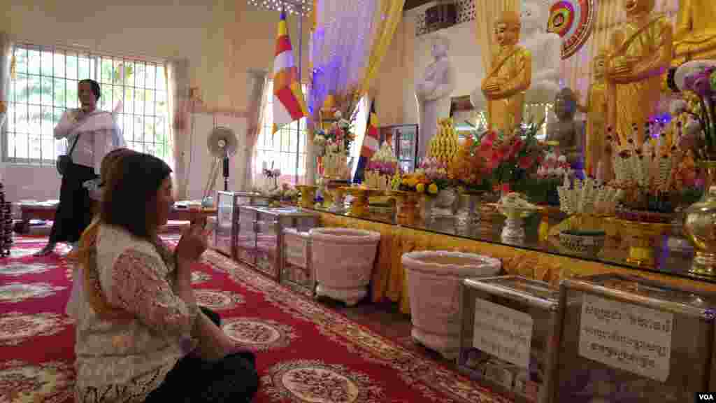 ស្ត្រីពីរនាក់បួងសួងនៅមុខរូបសំណាកព្រះពុទ្ធ នៅក្នុងវត្តសំពៅមាស ក្នុងរាជធានីភ្នំពេញ នៅថ្ងៃកាន់បិណ្ឌទី៥ (ថ្ងៃទី២១ ខែកញ្ញា ឆ្នាំ២០១៦)។ (ប៊ុន ប៉េងហ៊ុយ/VOA)