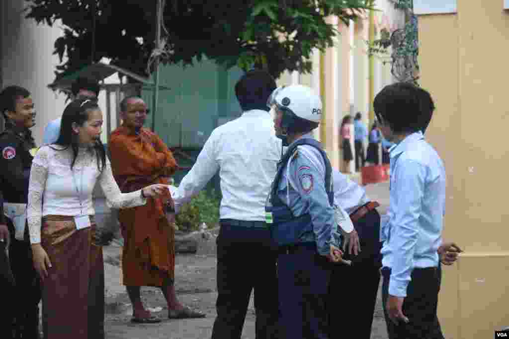 នគរបាលកំពុងឈររក្សាសន្តិសុខ ខណៈអនុរក្សកំពុងឈរចាំត្រួតពិនិត្យបេក្ខជនមុននឹងអនុញ្ញាតឱ្យចូលក្នុងមណ្ឌលប្រលងវិទ្យាល័យព្រះស៊ីសុវត្ថិ កាលពីថ្ងៃទី២៤ សីហា ឆ្នាំ២០១៥។ (ស៊ូ ពិសែន/VOA)