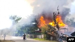 This handout taken on September 10, 2021 and received courtesy of an anonymous source on September 18 shows people attempting to extinguish a fire as houses burn in Namg Kar village in Magwe region's Gangaw township.
