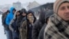 Migrants wait in line to receive plates of free food during a snowfall outside a derelict customs warehouse in Belgrade, Serbia, Jan. 18, 2017. 