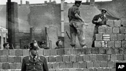 圖為1961年10月7日一名西柏林士兵站立在分割東、西柏林的混凝土牆邊。他身后為東柏林工人正在加高圍牆