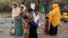 A family stands beside remains of a market which was set on fire, in Rohingya village outside Maungdaw, in Rakhine state, Myanmar, Oct. 27, 2016. 