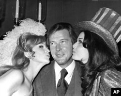 Roger Moore reçoit un baiser de Miss Grande Bretagne et de Miss USA à Londres, le 4 novembre 1971.