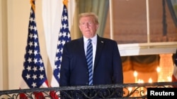 លោក​ប្រធានាធិបតី Donald Trump ឈរ​នៅ​រានហាល​ខាង​មុខ​នៃ​សេតវិមាន ដោយ​ដោះម៉ាស់ចេញ ក្រោ​យ​ត្រឡប់​ពី​ព្យាបាល​ជំងឺ​កូវីដ១៩ នៅ​មន្ទីរពេទ្យ​យោធា Walter Reed ថ្ងៃទី ៥ តុលា ឆ្នាំ២០២០។