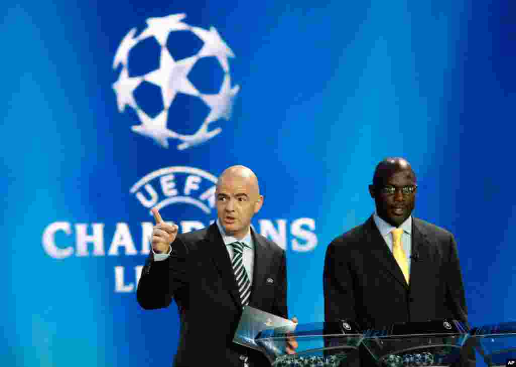 Le secrétaire général de l’UEFA Gianni Infantino à gauche fait geste alors que l’ancien footballeur libérien George Weah le regarde lors du tirage de la Champions League de l’UEFA à au forum Grimaldi, à Monaco, jeudi, le 30 aout 2014. Weah a annoncé sa candidat aux prochaines élections pour le Sénat après au Liberia.