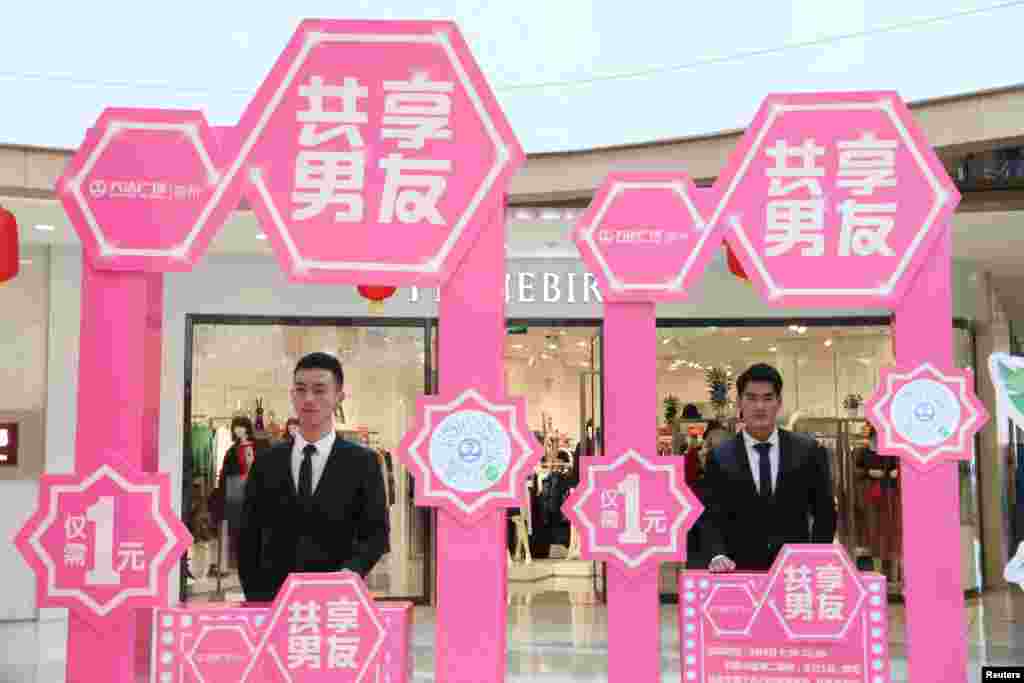 2018年3月8日,中国山东省滨州市,一个购物中心内的国际妇女节活动期间,男士站在展位后面,客户可以用一元人民币(0.16美元)租一个“男朋友”30分钟,帮自己拎包及提供导购服务,但不许离开商场,这吸引了许多女顾客围观。