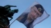 FILE - A man waves a flag showing Russian President Vladimir Putin in front of the monument of late Serbian Duke Mihailo Obrenovic in Belgrade, Serbia, Sept. 24, 2016.