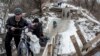 FILE - Local residents walk across a bridge damaged during fighting between Ukrainian government forces and Russia-backed rebels in Stanytsia Luhanska, Luhansk region, eastern Ukraine, Jan. 16, 2016.