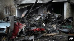 Les restes de l'hélicoptère mélangés à des débris, proches d'une voiture détruite sous le poids du métal.