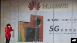 北京，一位戴著口罩的婦女站在華為手機廣告旁（2020年3月8日）。