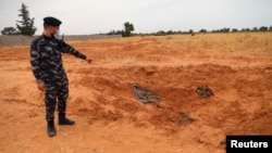 Un membre des forces de sécurité fidèles au GNA pointe vers une fosse commune à Tarhouna, en Libye, le 11 juin 2020.