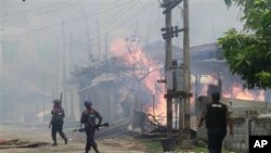 ရခိုင်ပြည်နယ် စစ်တွေမြို့မှာ မီးလောင်နေတဲ့ အိမ်တွေဘက် လုံခြုံရေး ရဲတပ်ဖွဲ့ဝင်တွေ အပြေးအလွှားသွားနေစဉ် (၁၂ ဇွန် ၂၀၁၂)