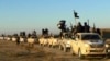 FILE - In this undated file photo released by a militant website, which has been verified and is consistent with other AP reporting, militants of the Islamic State group hold up their weapons and wave flags on their vehicles in a convoy on a road leading leading to Iraq, while riding in Raqqa, Syria. 
