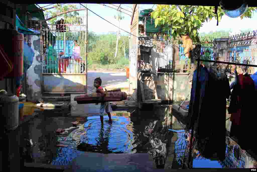 ក្មេងស្រីម្នាក់ ឈរកាន់កន្ទេលក្នុងទឹកដែលលិចនៅមុខផ្ទះរបស់លោក ឃឹន សុវាត ដែលស្ថិតនៅក្នុងតំបន់បឹងកក់ ក្នុងទីក្រុងភ្នំពេញនៃប្រទេសកម្ពុជា នៅថ្ងៃទី១៣ ខែវិច្ឆិកា ឆ្នាំ២០១៤។ (នូវ ពៅលក្ខិណា)