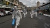 Workers wearing personal protective equipment (PPE) carry disinfectant to be sprayed at the Orussey market, after it was temporarily closed following a few vendors testing positive for the Covid-19 coronavirus, in Phnom Penh on April 4, 2021. (Photo by TANG CHHIN Sothy / AFP)