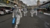 FILE - Workers wearing personal protective equipment (PPE) carry disinfectant to be sprayed at the Orussey market, after it was temporarily closed following a few vendors testing positive for the Covid-19 coronavirus, in Phnom Penh on April 4, 2021. (AFP)